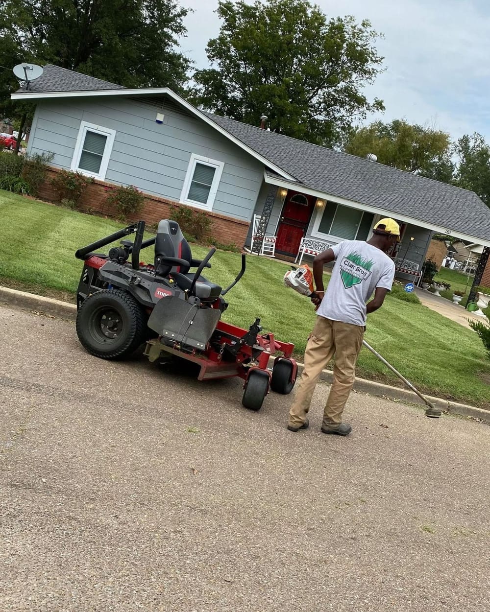 A Clark Bros crew member in a company shirt trimming a front lawn beside the mower