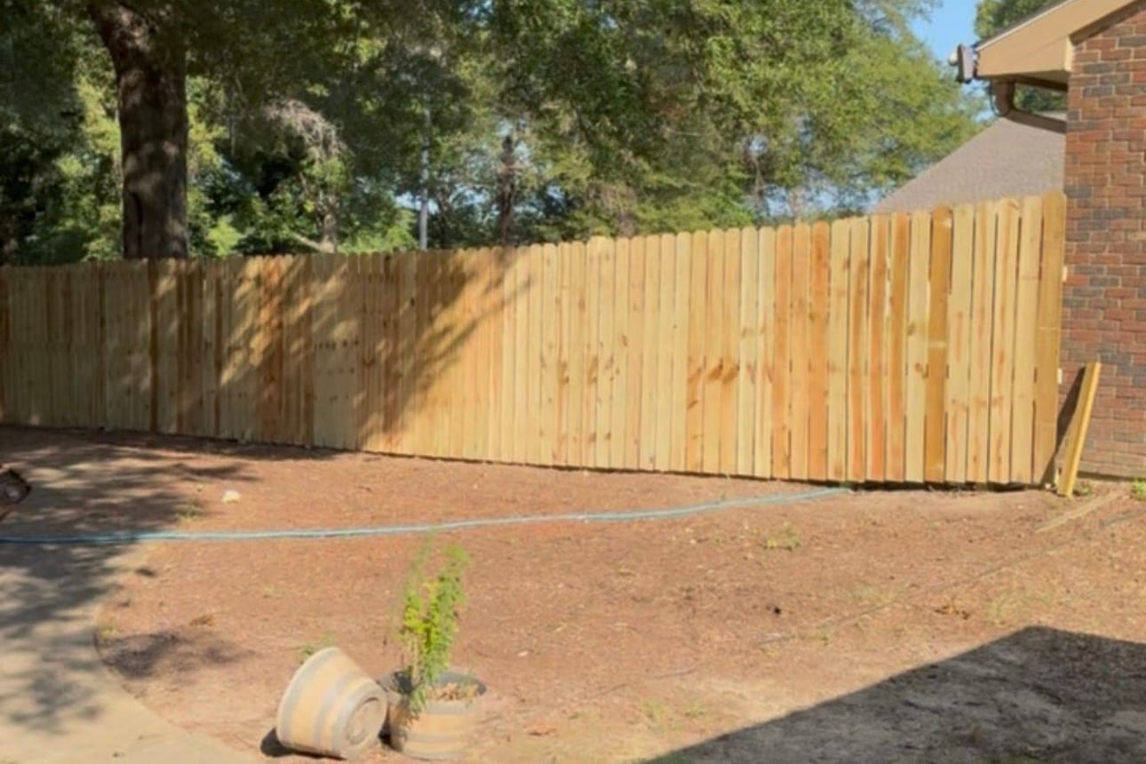 A new dog-ear privacy fence meeting the corner of a brick house, boards freshly installed