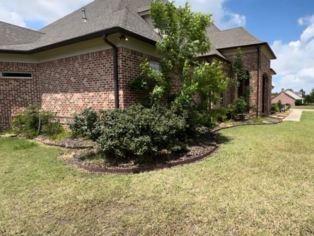 A mulched planting bed curving around the corner of a brick house with a crisp edge against the lawn